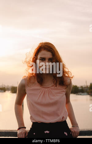 Portrait of young serious woman standing on bridge at sunset Stock Photo