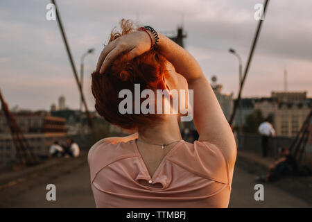 Rear view of young woman holding hair while walking on bridge in city Stock Photo