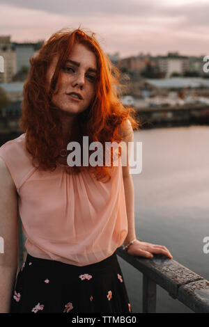 Portrait of redhead teenage girl standing by railing on bridge in city Stock Photo
