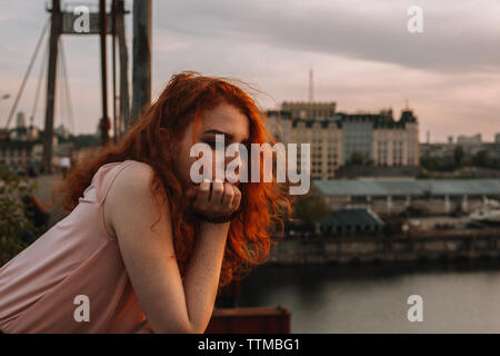 Portrait of thoughtful red haired girl leaning on railing at bridge Stock Photo