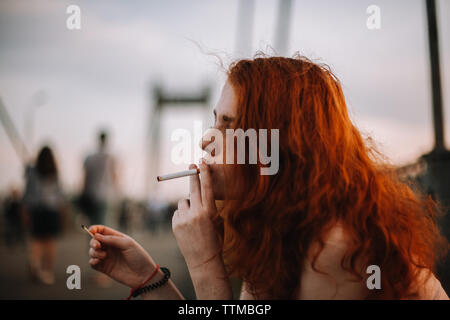 Young woman smoking cigarette while holding matchstick in hand Stock Photo