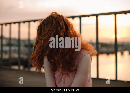 Red head woman tossing hair while sitting on bridge at sunset Stock Photo