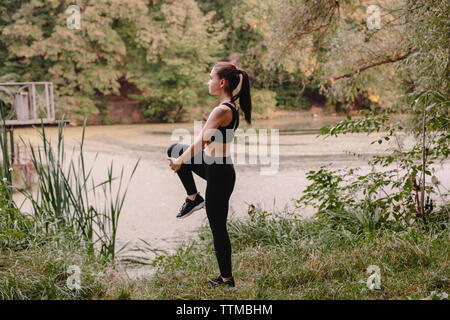 Side view of female jogger stretching at lakeshore in park Stock Photo