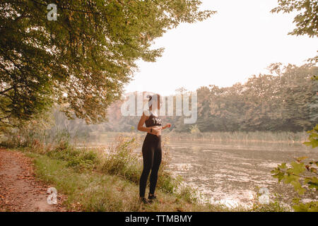 Female jogger standing by lake in forest Stock Photo