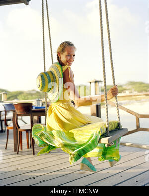 Aruba, Surfside Marina, a young woman sits on a swing smiling at Pinchos Bar & Grill Stock Photo