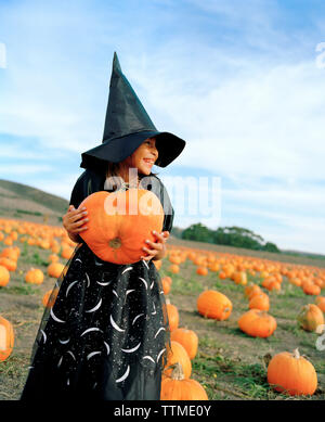 USA, California, young girl dressed as a witch holding a pumpkin at Bob's Pumpkin Patch, Half Moon Bay Stock Photo