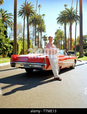 USA, California, Beverly Hills, a man stands in the street leaning on his red convertible Cadillac Stock Photo