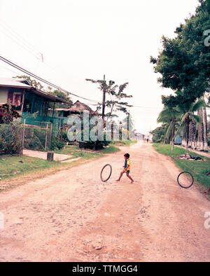 PANAMA, Bocas del Toro, a young boy rolls and plays with bicycle tires in the street, Central America Stock Photo
