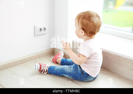 Baby playing with electrical outlet on floor at home Stock Photo
