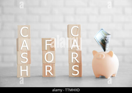 Cubes with words CASH FOR CARS and piggy bank on brick wall background Stock Photo