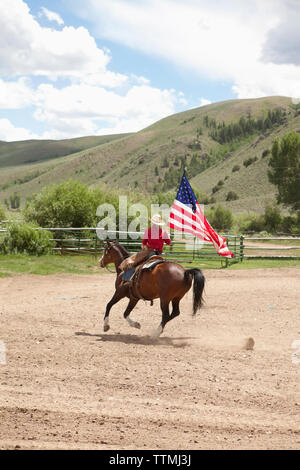 USA, Wyoming, Encampment, a young man rides his horse carrying the American flag, Abara Ranch Stock Photo