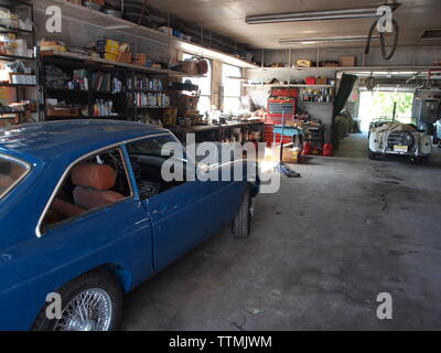 Interior of a British car restoration garage in Tuxedo, New York showing a blue MGB-GT in foreground being restored. Natural light illuminates cars. Stock Photo