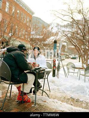 USA, Colorado, Aspen, couple wearing ski gear having coffee at an outdoor table in the Winter in downtown Stock Photo