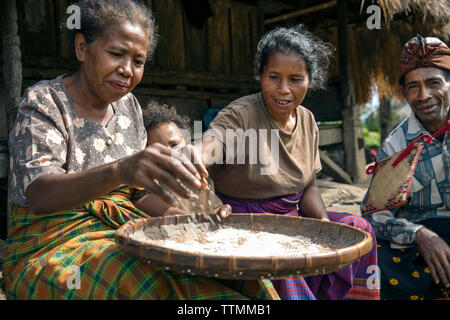 INDONESIA, Flores, a family sorts through rice in front of their home in Kampung Tutubhada village in Rendu Stock Photo