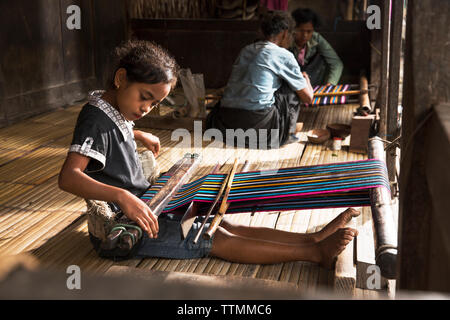 INDONESIA, Flores, 5th grader Santi Itu weaves and chews Betel Nut in front of her home at Bena village Stock Photo