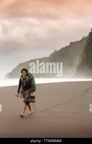 USA, Hawaii, The Big Island, backpacker walks on the beach along the surf in the Waipio Valley Stock Photo