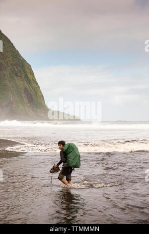 USA, Hawaii, The Big Island, backpacker walks on the beach along the surf in the Waipio Valley Stock Photo