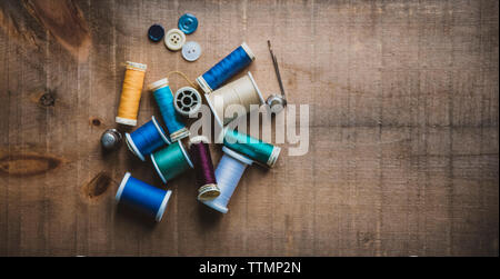 High angle view of colorful spools with thimbles and buttons on wooden table at workshop Stock Photo