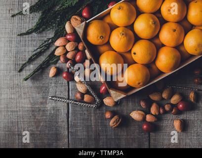 High angle view of oranges in box by various dry fruits and nutcracker on wooden table Stock Photo