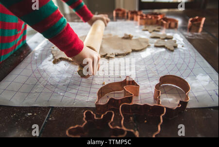 Close-up of boy rolling cookie dough on table during christmas at home Stock Photo