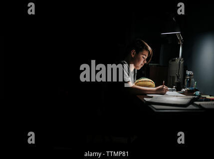 Side view of boy studying at table in darkroom Stock Photo