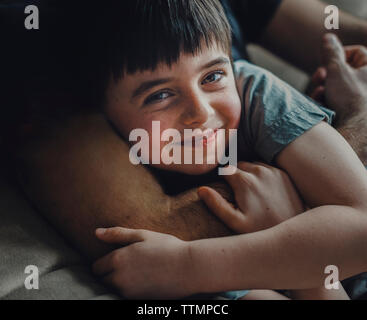 Midsection of father embracing happy son while lying on sofa at home Stock Photo