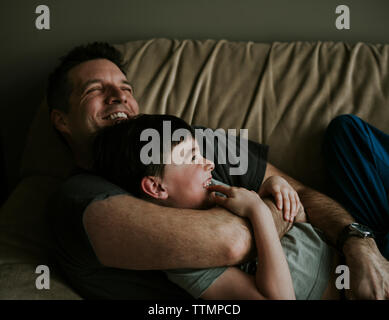 Happy father embracing son while lying on sofa at home Stock Photo