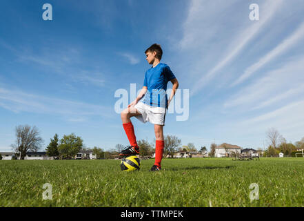 Low angle view of boy with soccer ball standing on grassy field Stock Photo