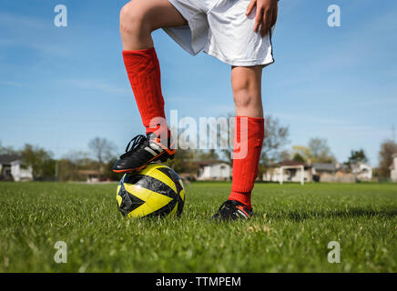 Low section of boy with soccer ball standing on grassy field against sky Stock Photo