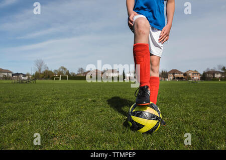 Low section of boy with soccer ball standing on grassy field Stock Photo