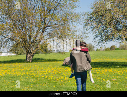 Rear view of father carrying son with broken leg on grassy field at park Stock Photo
