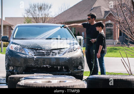 Father washing car while standing by son on driveway Stock Photo