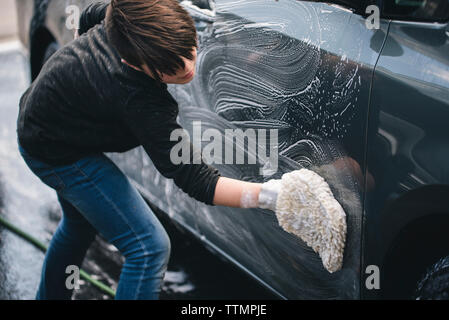 Side view of boy washing car on driveway Stock Photo