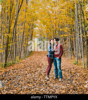 Man kissing happy woman while standing on dry leaves in forest during autumn Stock Photo