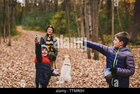 Boy with dog looking at brothers feeding birds in forest during autumn Stock Photo