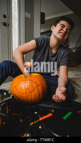 Boy removing seeds from pumpkin while sitting on floor at home Stock Photo