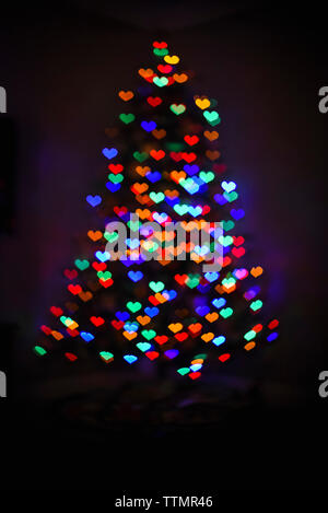 Colorful heart shaped light bokeh on a Christmas tree in the dark. Stock Photo