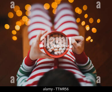 Child wearing Christmas pjs holds cup of hot cocoa with marshmalows.l Stock Photo