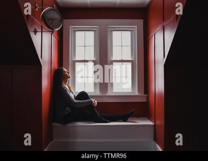 Woman sitting and relaxing in window alcove with eyes closed. Stock Photo