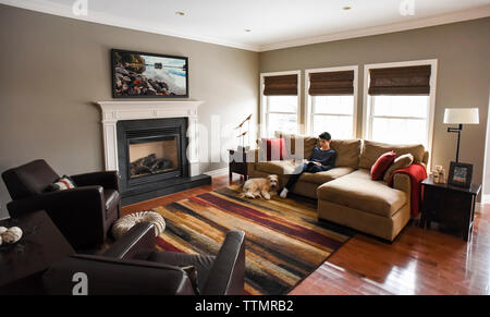 Boy reading on couch in living room with dog in the daytime. Stock Photo