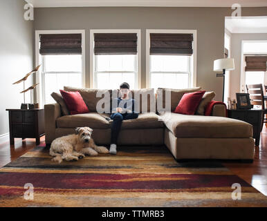 Boy reading on couch in living room with dog in the daytime. Stock Photo