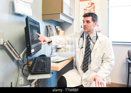 Doctor in white coat pointing at computer screen in a clinic room. Stock Photo