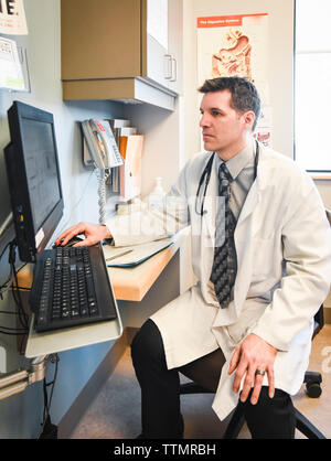 Doctor in white coat using a computer in a clinic room. Stock Photo