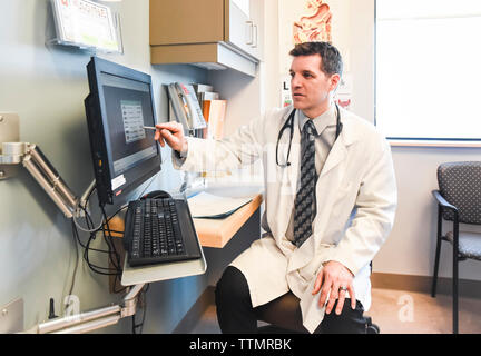 Doctor in white coat pointing at computer screen in a clinic room. Stock Photo