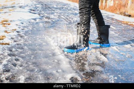 Cropped close up of rubber boots splashing in a slushy puddle. Stock Photo