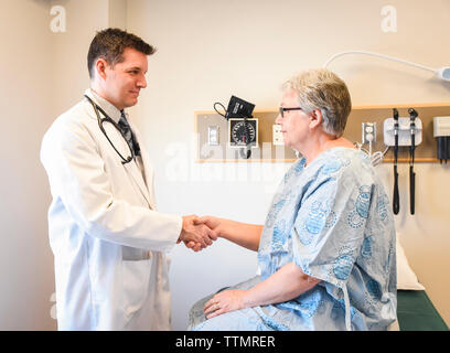 Doctor shaking hands with older patient wearing gown in clinic. Stock Photo