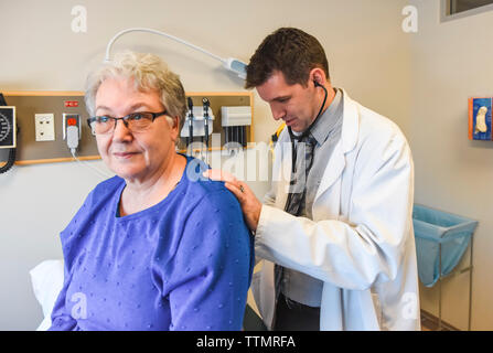Doctor listening to lungs of older patient with stethoscope in clinic. Stock Photo