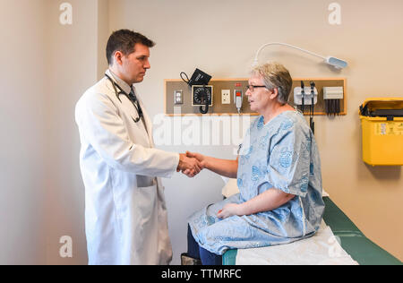 Doctor shaking hands with older patient in gown in clinical setting. Stock Photo