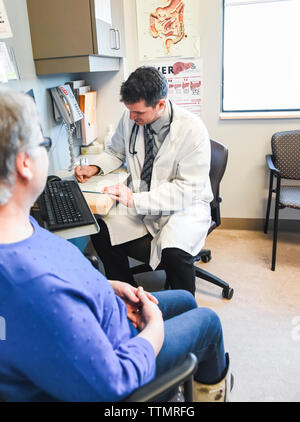 Doctor taking patient history from older woman at a desk in a clinic. Stock Photo