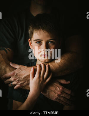 Close up portrait of serious boy with father's arms around him. Stock Photo
